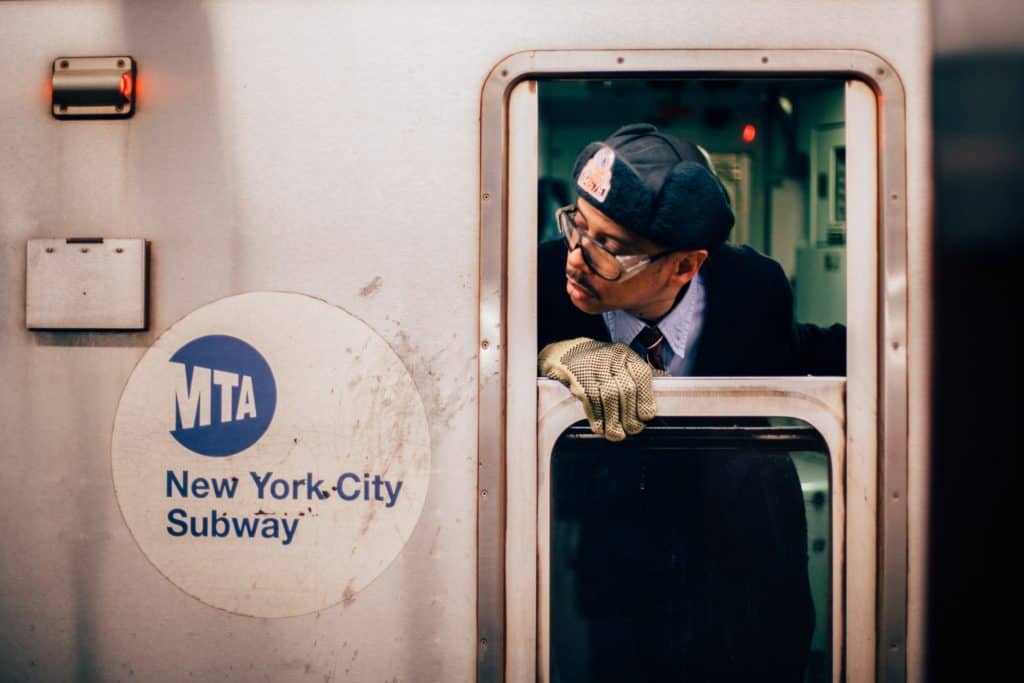 An image of a conductor leaning out the window of a subway train in New York City