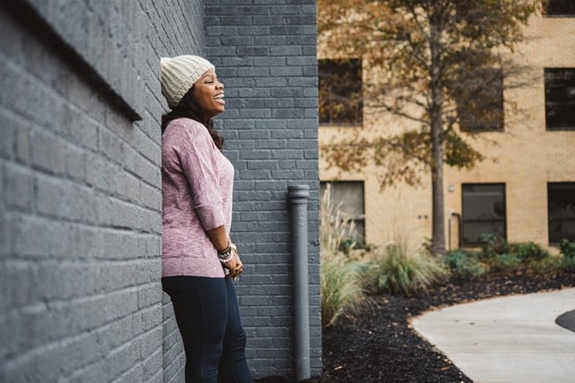 woman standing against a brick wall laughing on a fall day