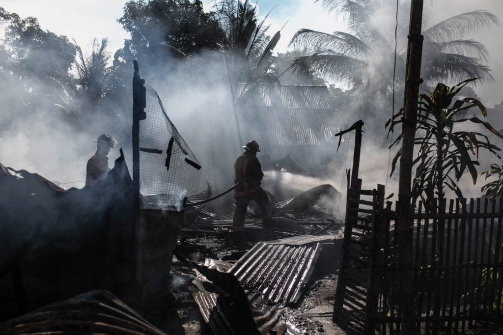 firefighter puts out a fire with palm trees and smoke filling up the background
