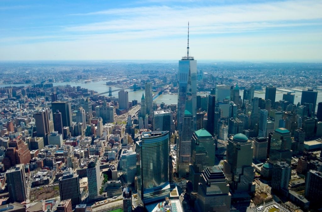 lower manhattan, with one world trade center towering above the rest of the buildings in the center of the photo